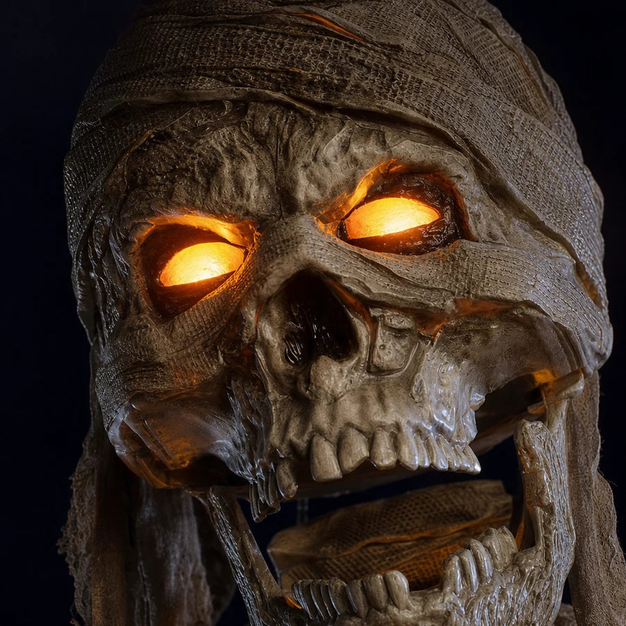 Close-up of the wrapped skull face, both eye sockets glowing amber-orange in the dark