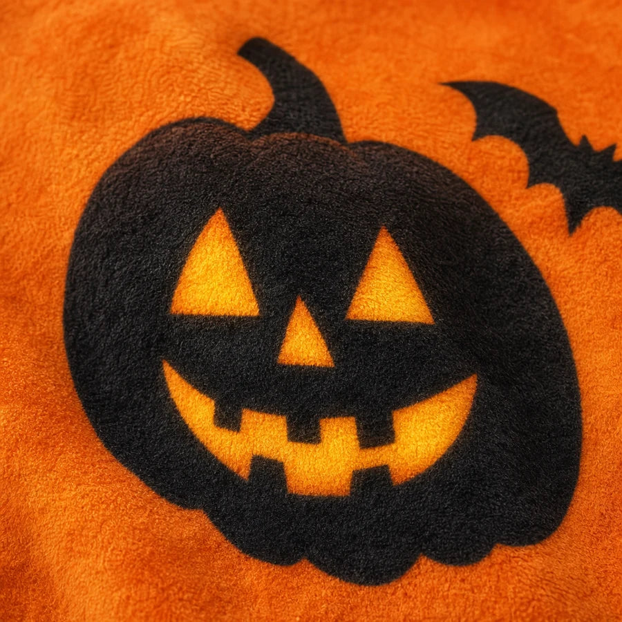 Close on one glowing jack-o'-lantern in the print, amber eyes and mouth lit